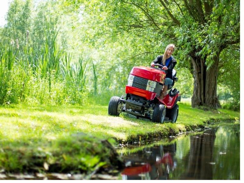 lady on ride-on lawnmower at the edge of water